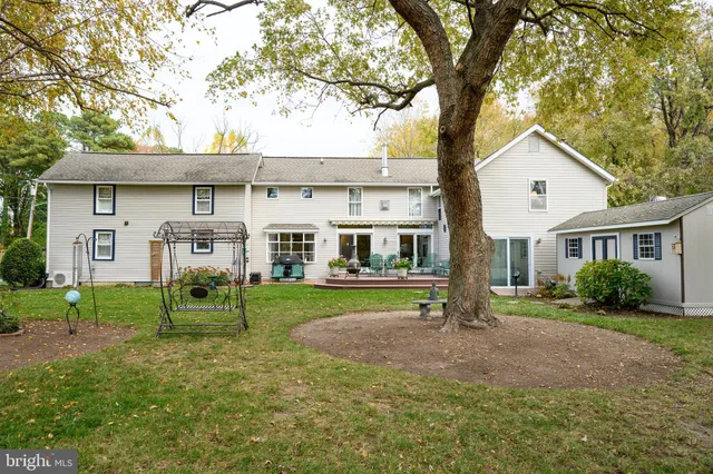 a view of house in front of a big yard with large trees and wooden fence