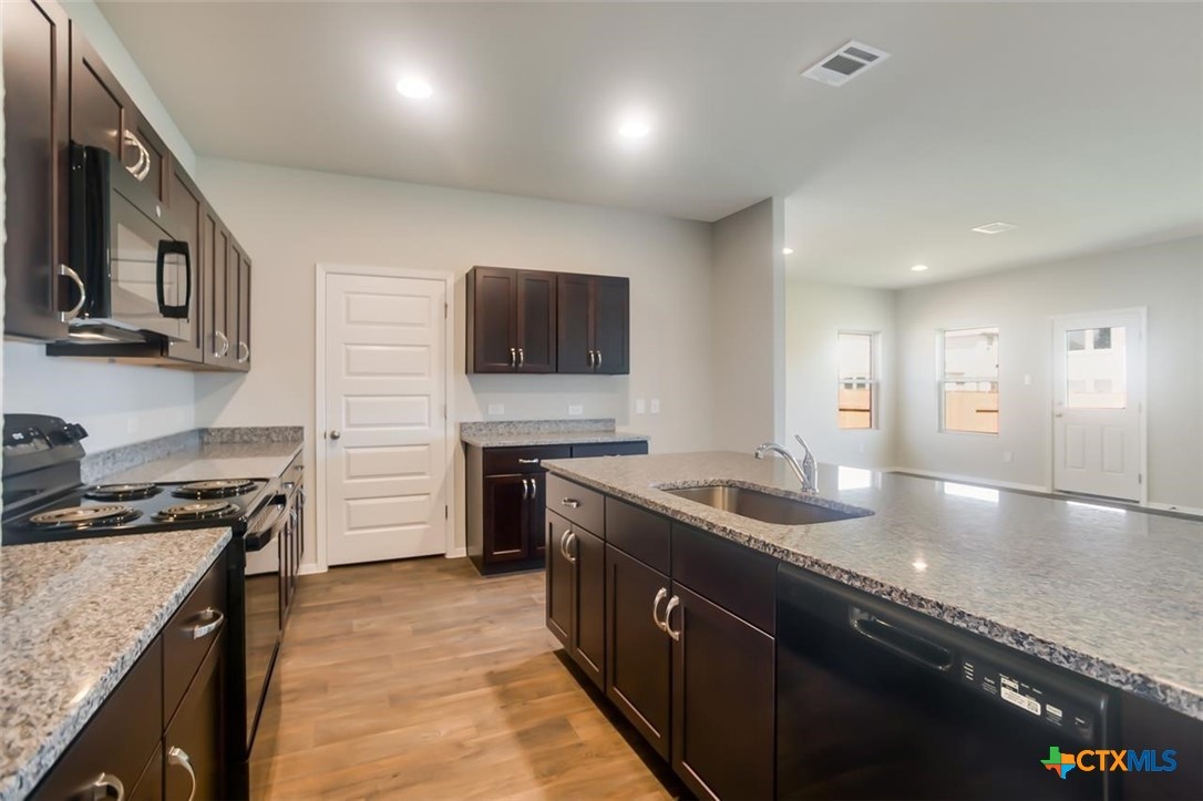 2428 Ambling Trail Georgetown, TX 78628 - Photo 6 of 33 a kitchen with granite countertop a sink and a stove top oven with wooden floor