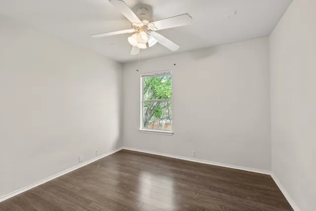 an empty room with wooden floor window and ceiling fan