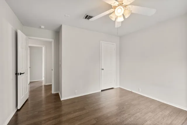 a view of an empty room with wooden floor and a ceiling fan