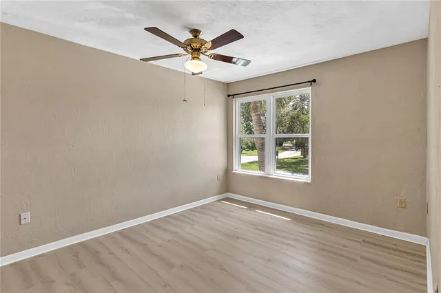 an empty room with wooden floor fan and windows
