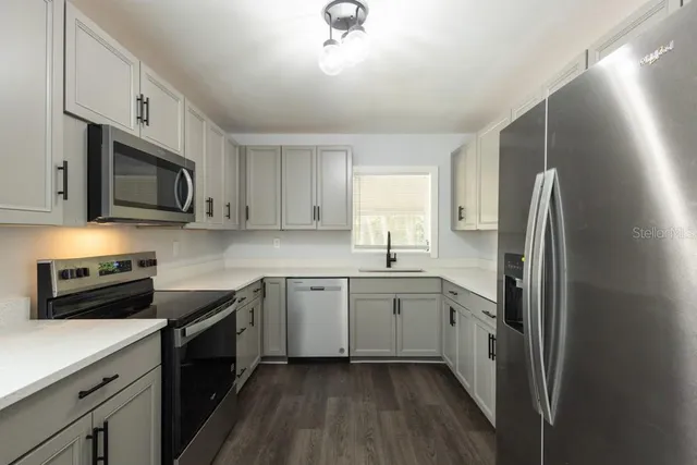 a kitchen with stainless steel appliances granite countertop white cabinets a sink a stove a refrigerator and microwave with wooden floor