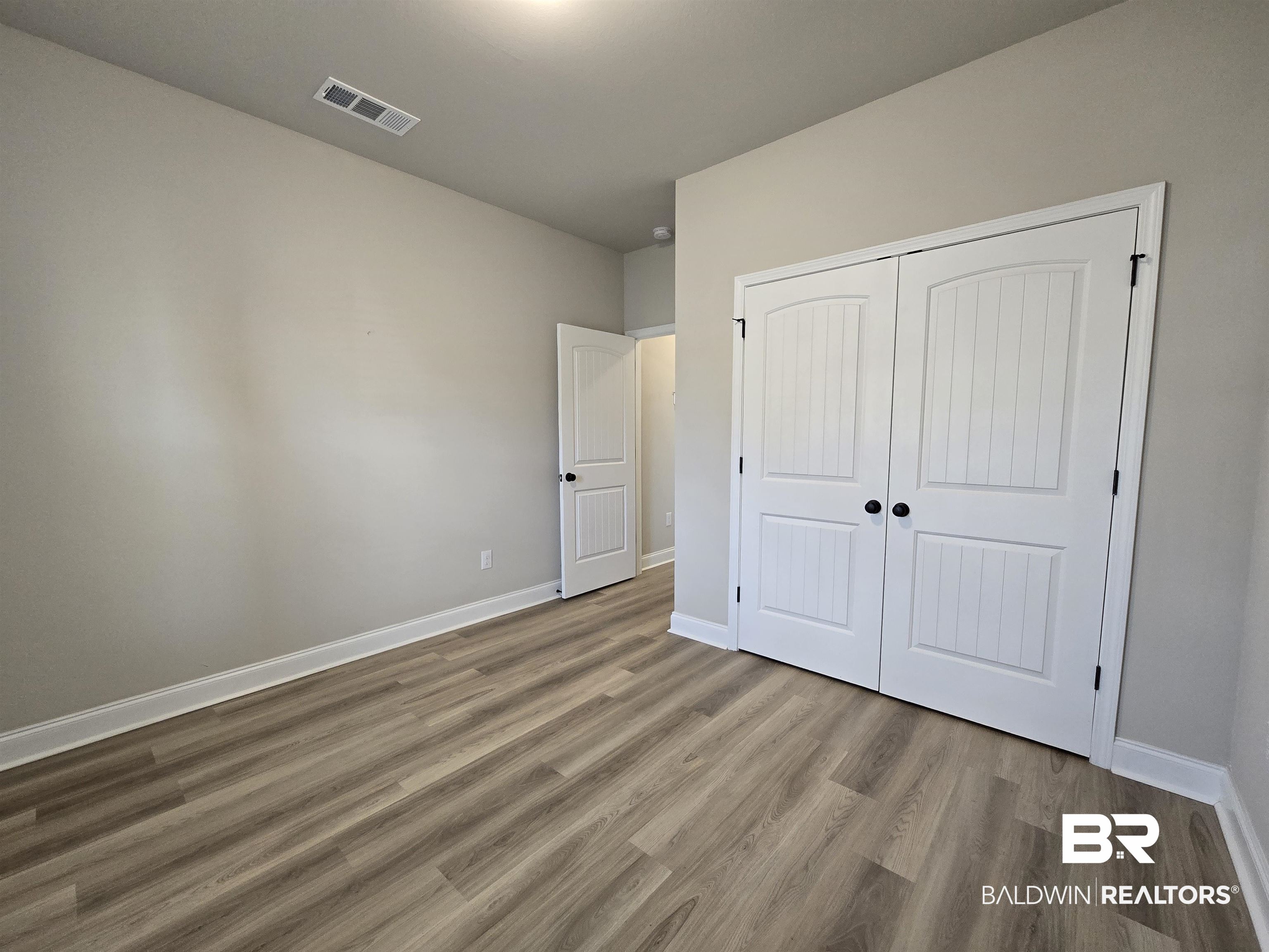 1060 Chloe Street Foley, AL 36535 - Photo 22 of 28 Interior room featuring wood-finish flooring, light neutral wall paint, white baseboards, and white bi-fold closet doors with black hardware