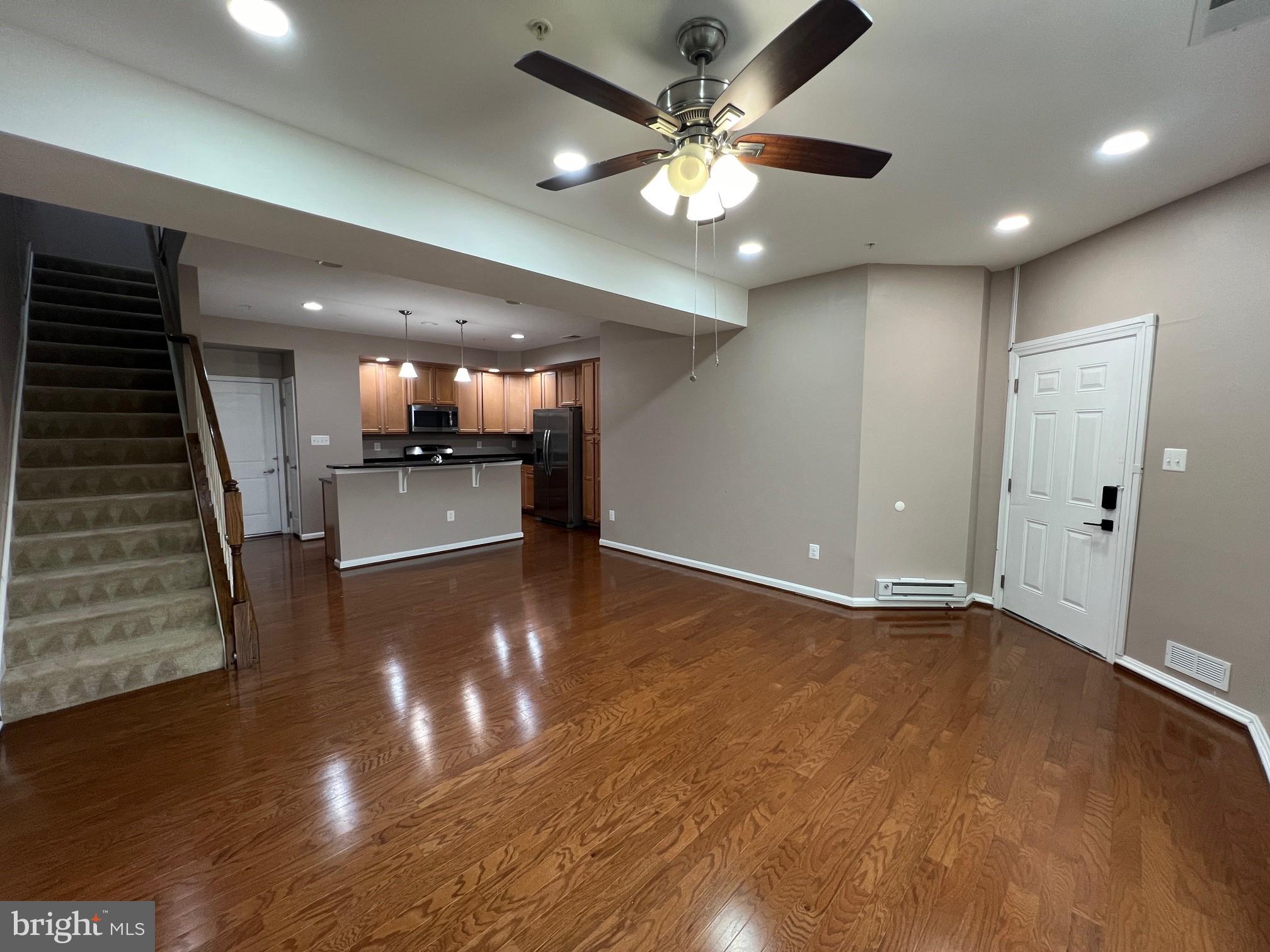 5057 Small Gains Way Frederick, MD 21703 - Photo 4 of 22 an empty room with wooden floor ceiling fan and kitchen view