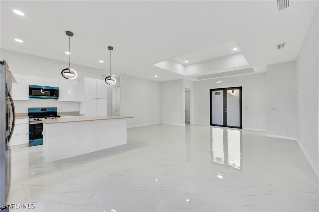 347 Ranch Avenue Lehigh Acres, FL 33974 - Photo 6 of 30 a large white kitchen with kitchen island a refrigerator a stove a microwave and white cabinets with wooden floor