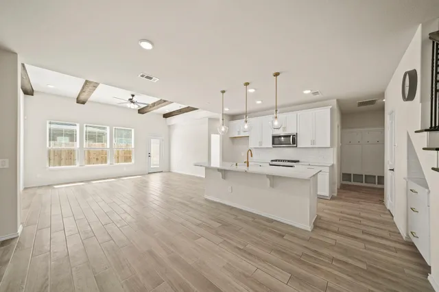 a large kitchen with kitchen island a stove a sink dishwasher a refrigerator and white cabinets with wooden floor