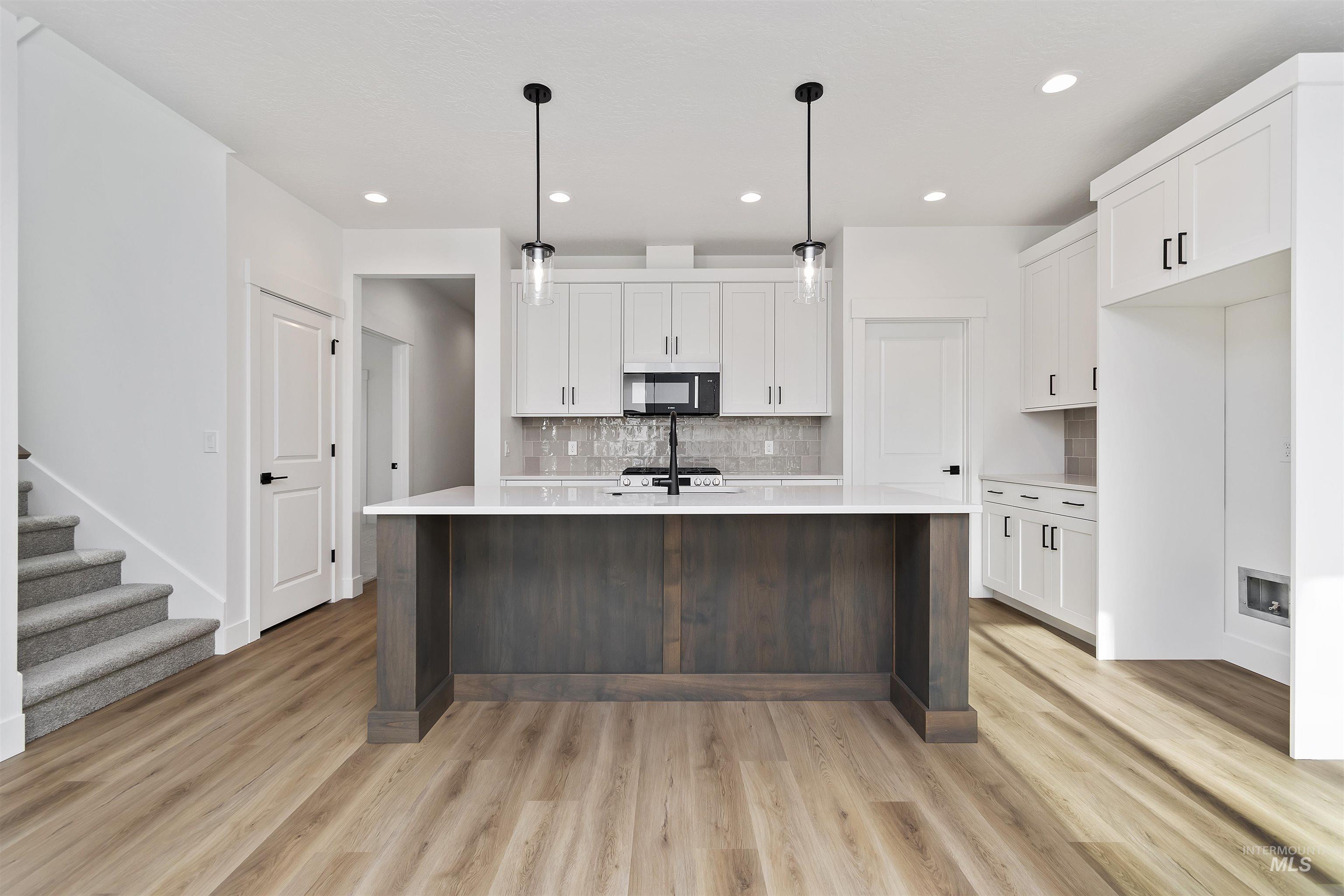732 South Calhoun Lane Star, ID 83669 - Photo 7 of 48 Kitchen featuring white cabinets, decorative light fixtures, an island with sink, tasteful backsplash, and light wood-type flooring