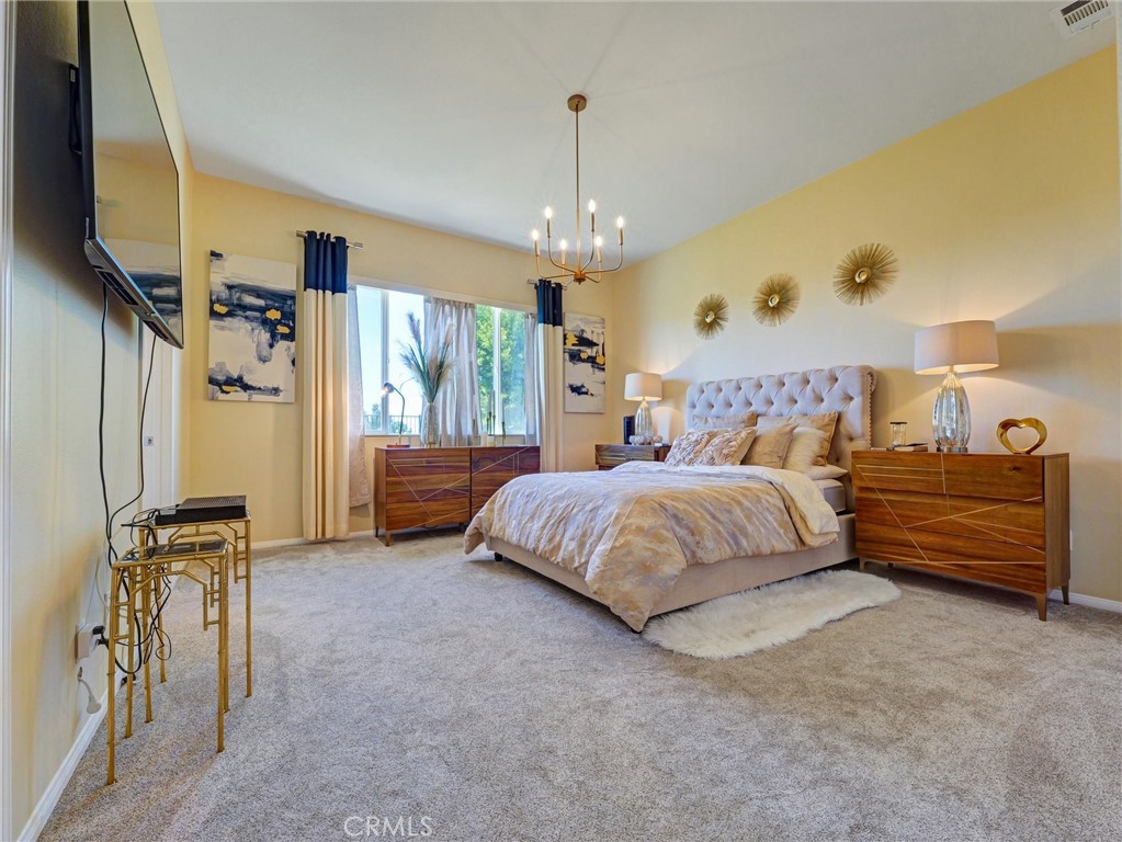887 Westchester Road Beaumont, CA 92223 - Photo 26 of 41 a spacious bedroom with a bed a chandelier and a flat screen tv