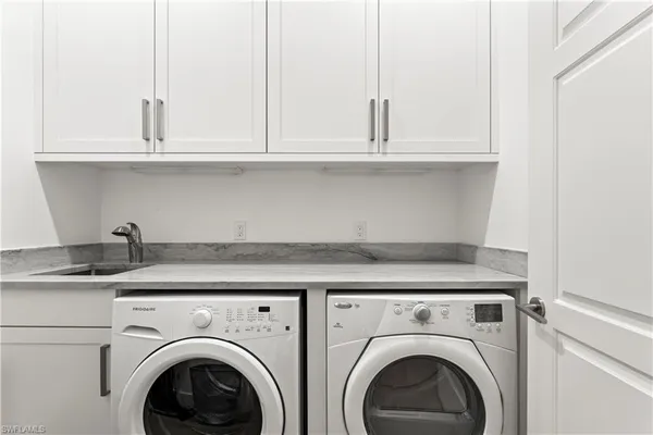a utility room with granite countertop stainless steel appliances white cabinets and a sink