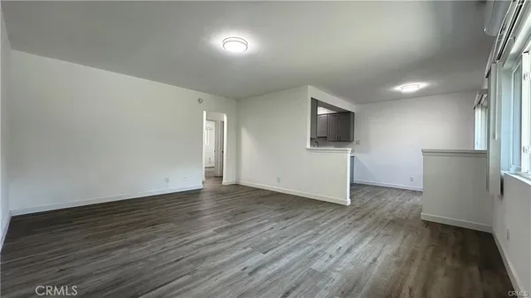 an empty room with wooden floor and way to kitchen