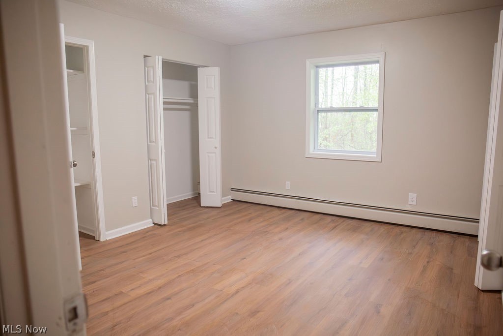 3644 Padanarum Road Geneva, OH 44041 - Photo 9 of 19 Spacious room featuring wood-finish flooring, neutral wall tones, baseboard heating, and two bi-fold door closets