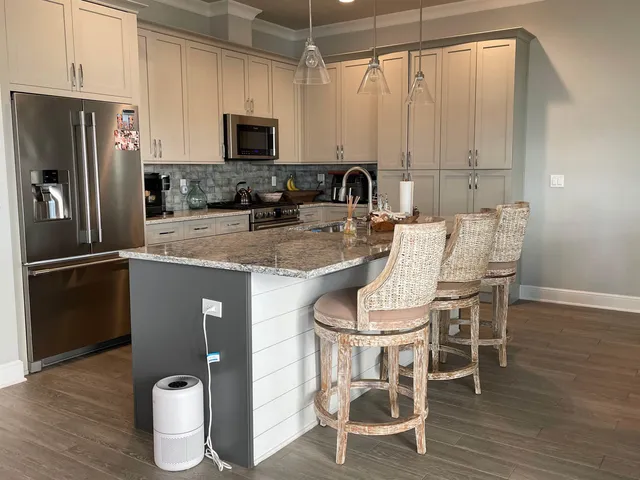 a kitchen with stainless steel appliances granite countertop a refrigerator a stove a sink and white cabinets with wooden floor