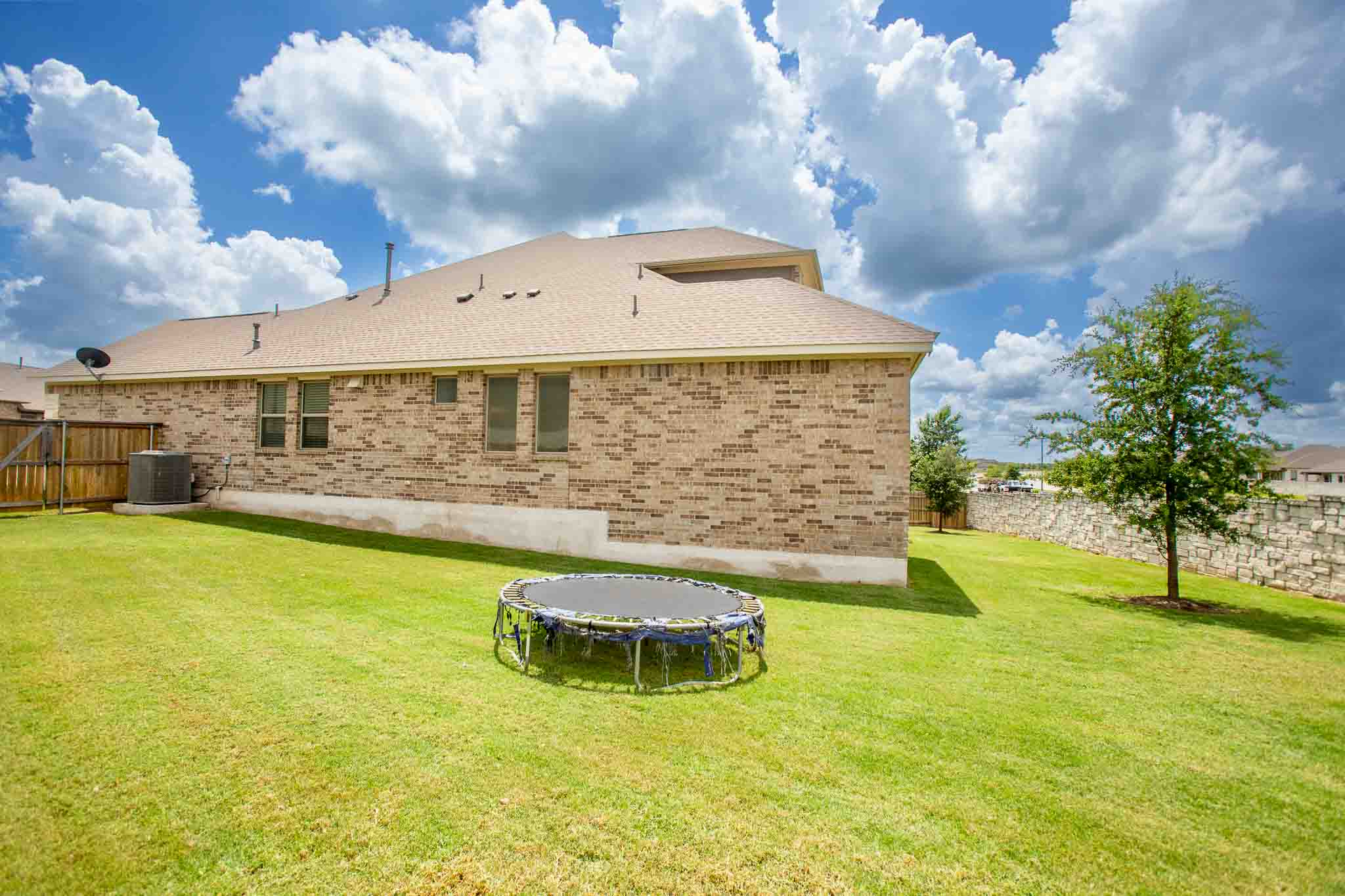 166 West Branch Road Kyle, TX 78640 - Photo 38 of 39 A well-maintained lawn stretches beside a brick-clad residence, featuring a stone wall accentuating the perimeter.