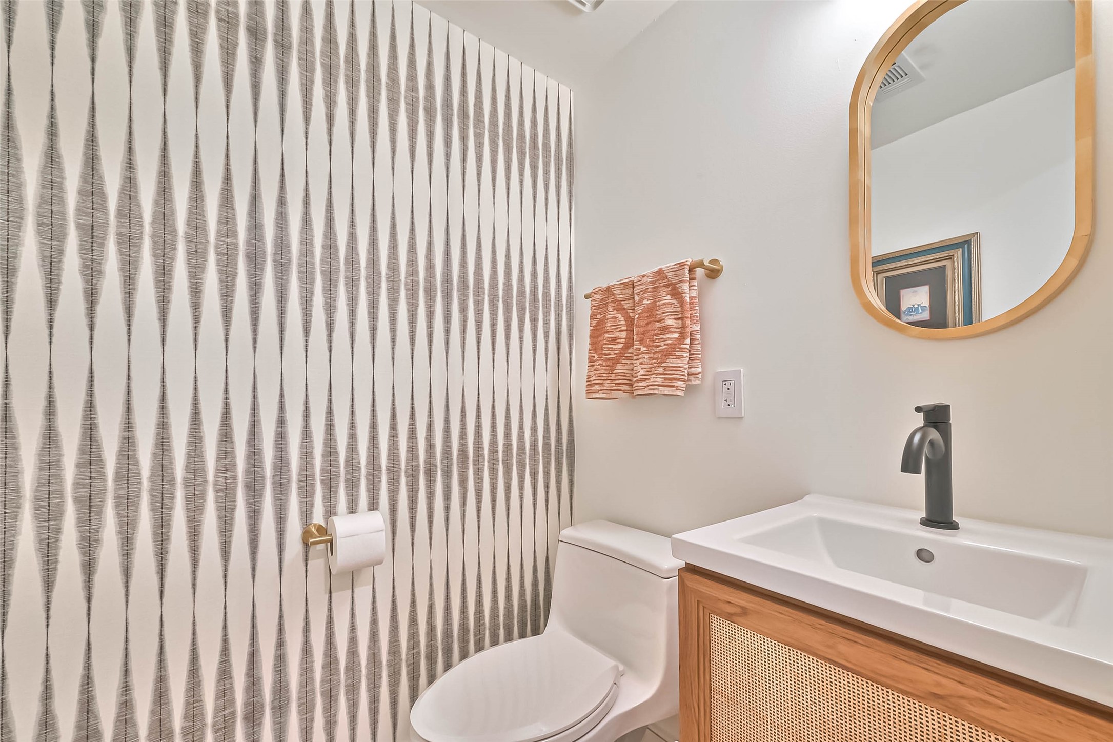 412 Sue Street Houston, TX 77009 - Photo 8 of 19 This downstairs half bathroom features a modern design with a striking geometric wallpaper, a sleek black faucet, and a wooden-framed mirror, creating a contemporary and stylish space.