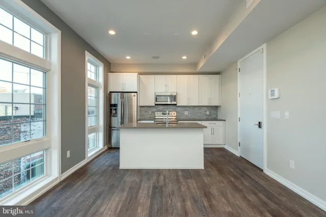 a kitchen with stainless steel appliances granite countertop a refrigerator a sink dishwasher a stove and white countertops with wooden floor