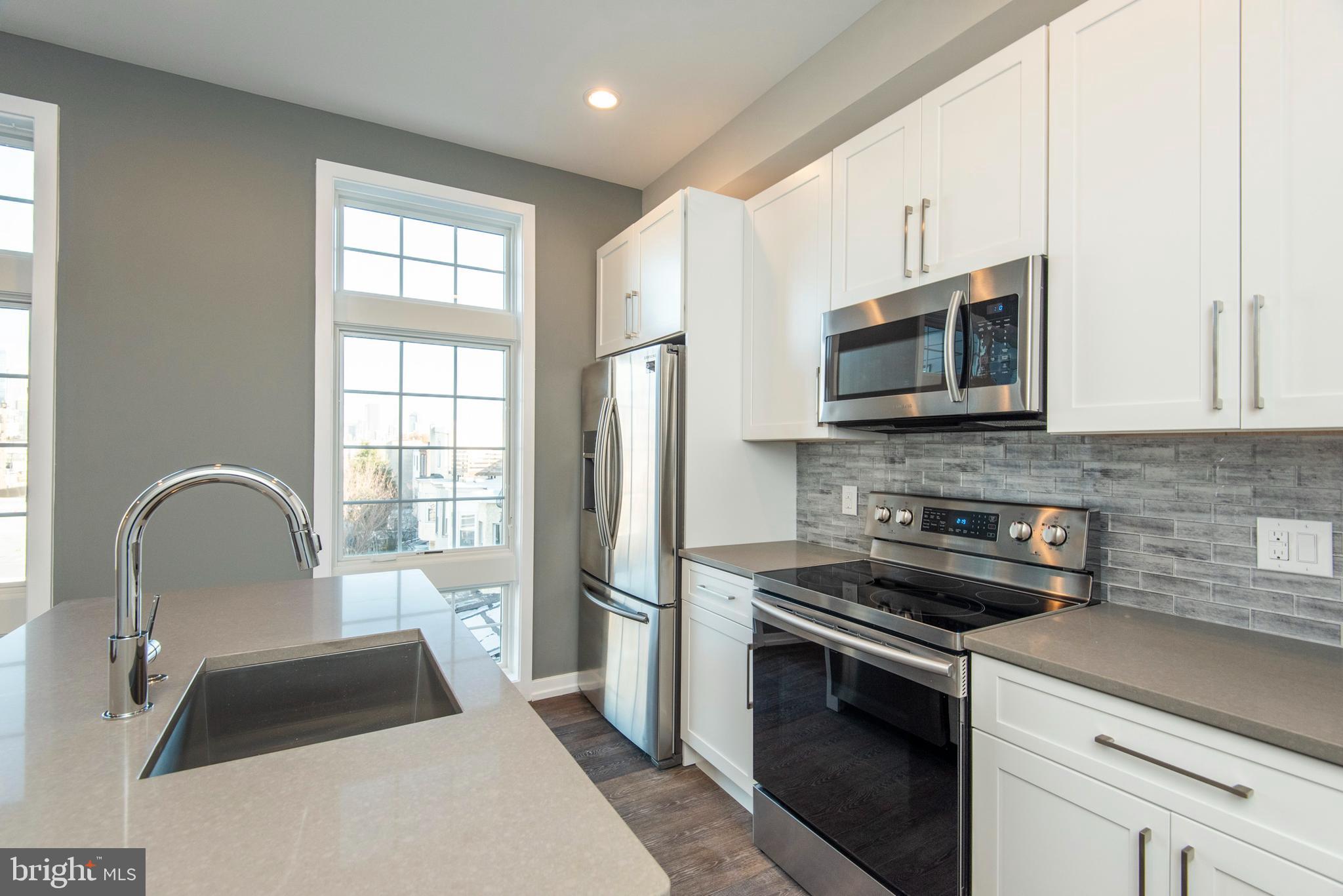 1340 South 13th Street, Unit 3B Philadelphia, PA 19147 - Photo 8 of 31 a kitchen with a microwave a stove a sink dishwasher a refrigerator with white cabinets and wooden floor