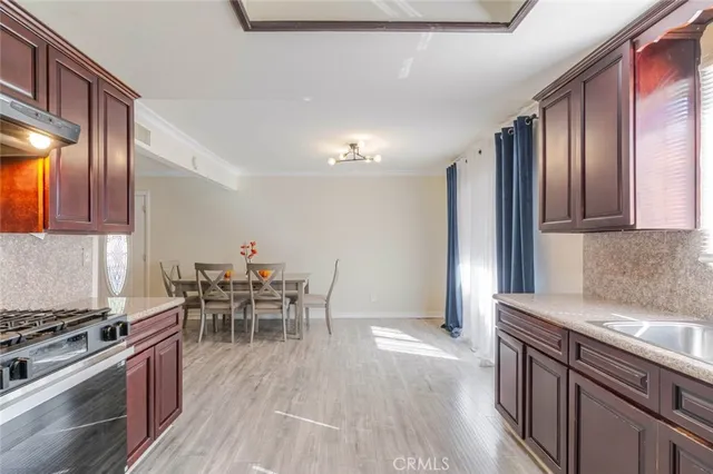 a kitchen with stainless steel appliances granite countertop a stove top oven a sink a dining table and chairs with wooden floor