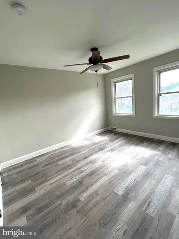 an empty room with wooden floor ceiling fan and windows