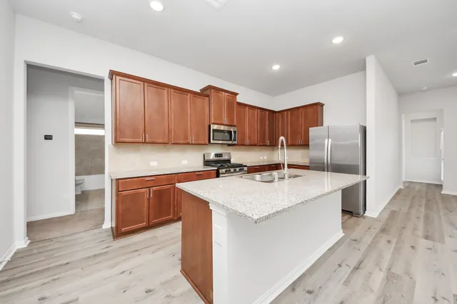 a kitchen with stainless steel appliances granite countertop a sink a stove a refrigerator and island with wooden floor