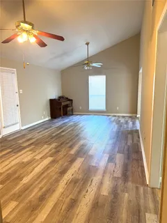 an empty room with wooden floor fan and windows