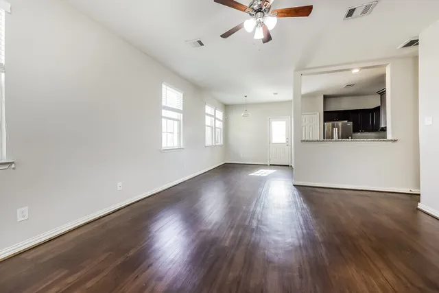 a view of an empty room with wooden floor and a ceiling fan
