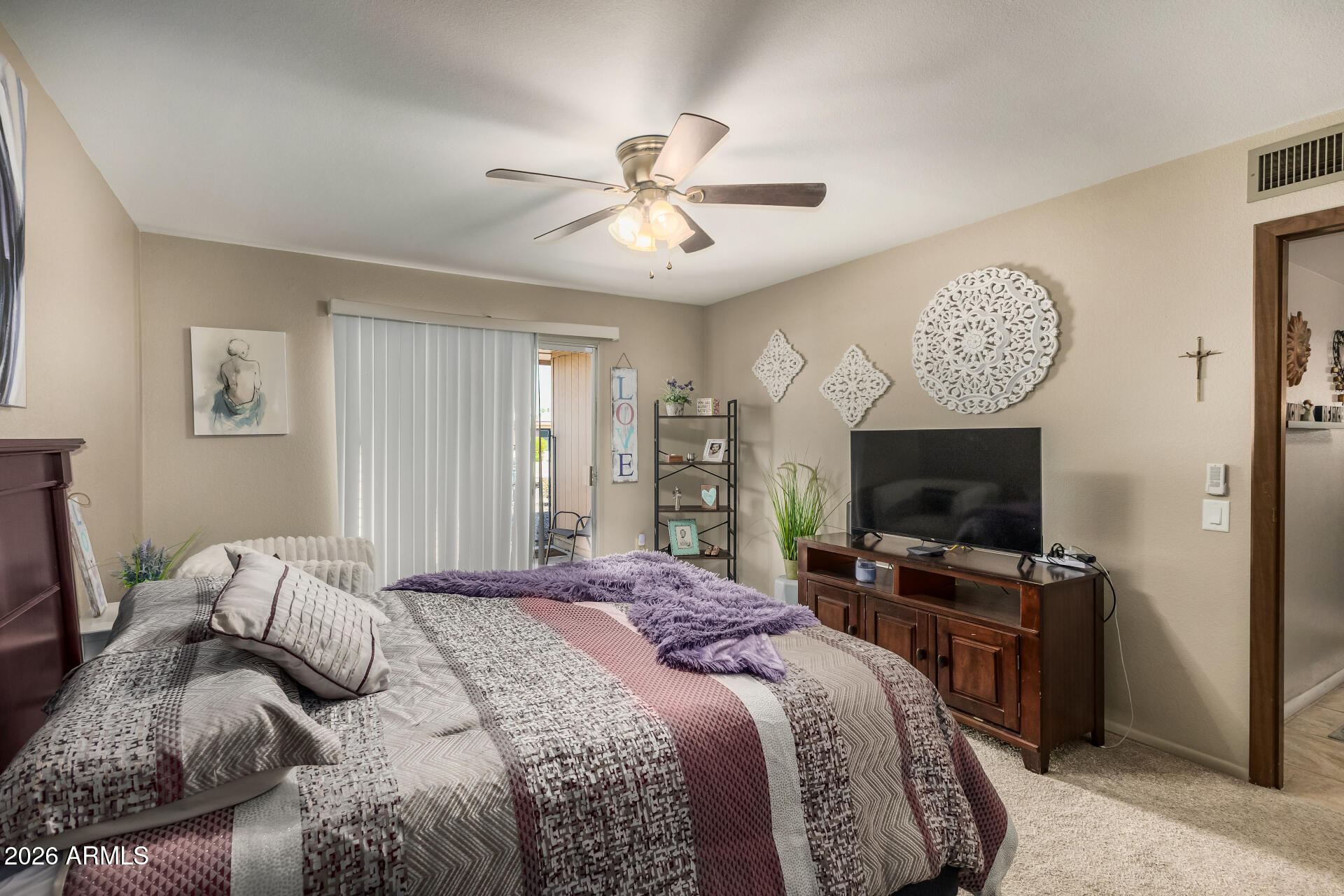 9845 West Royal Ridge Drive Sun City, AZ 85351 - Photo 18 of 28 a bedroom with a large bed a flat tv screen and a chandelier