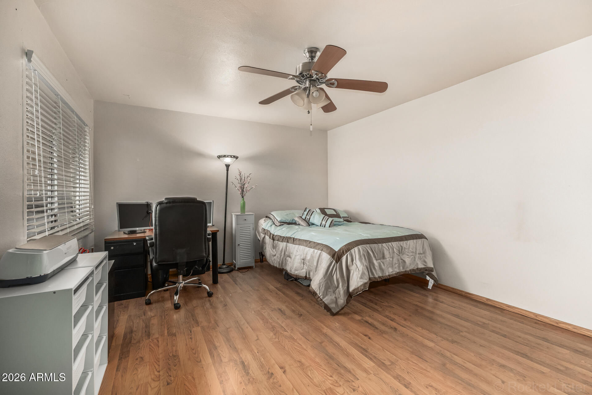 9845 West Royal Ridge Drive Sun City, AZ 85351 - Photo 21 of 28 a bedroom with a bed a desk and chair with wooden floor