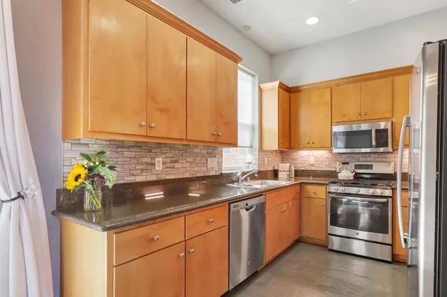 a kitchen with stainless steel appliances granite countertop a sink a stove a refrigerator cabinets and a window