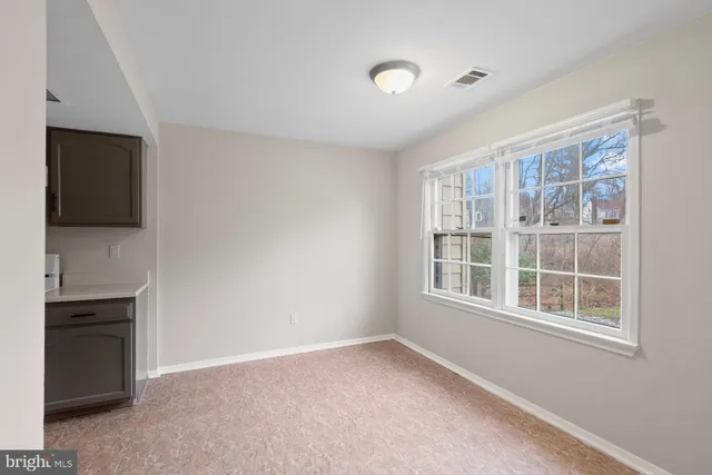 a view of an empty room with a window and kitchen view