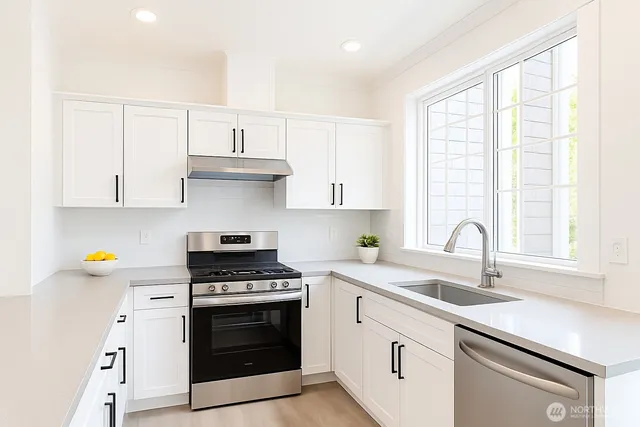 a kitchen with granite countertop a sink cabinets stainless steel appliances and a window