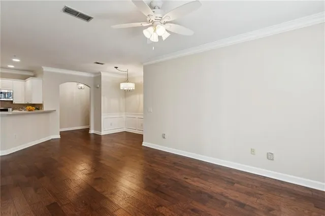a view of an empty room with wooden floor and a kitchen