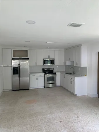 a kitchen with granite countertop a refrigerator and white cabinets