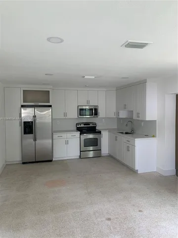 a kitchen with granite countertop a refrigerator and white cabinets
