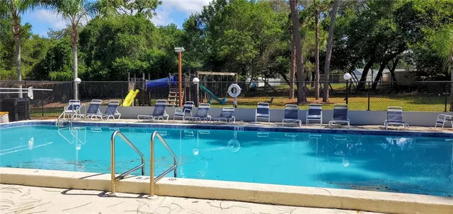 a view of a swimming pool with a bench and lawn chairs under an umbrella