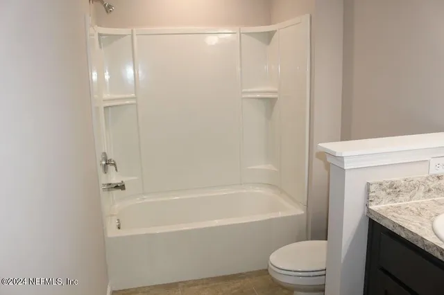 a bathroom with a granite countertop bathtub shower sink vanity and toilet