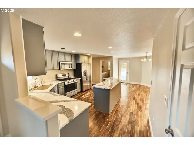 a living room with stainless steel appliances kitchen island granite countertop a table chairs and a refrigerator