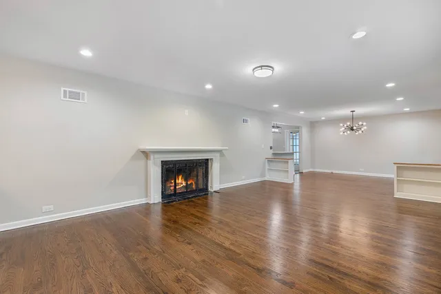 an empty room with wooden floor fire place and kitchen view