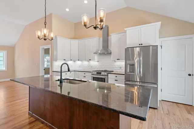 a kitchen with stainless steel appliances granite countertop a refrigerator a sink dishwasher a stove and a dining table with wooden floor