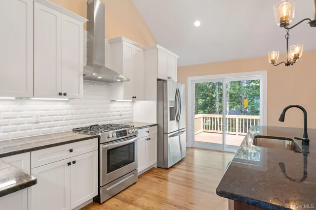 a kitchen with stainless steel appliances granite countertop a stove a sink dishwasher a refrigerator white cabinets and wooden floor