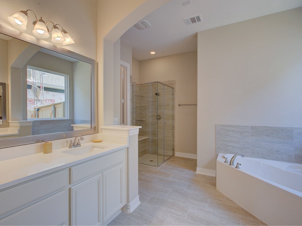 4303 Logan Ridge Drive Cedar Park, TX 78613 - Photo 10 of 24 Bathroom featuring a double vanity with white cabinetry and light-toned countertops, a frameless glass shower enclosure with tile surround, a built-in soaking tub, and neutral-toned tile flooring