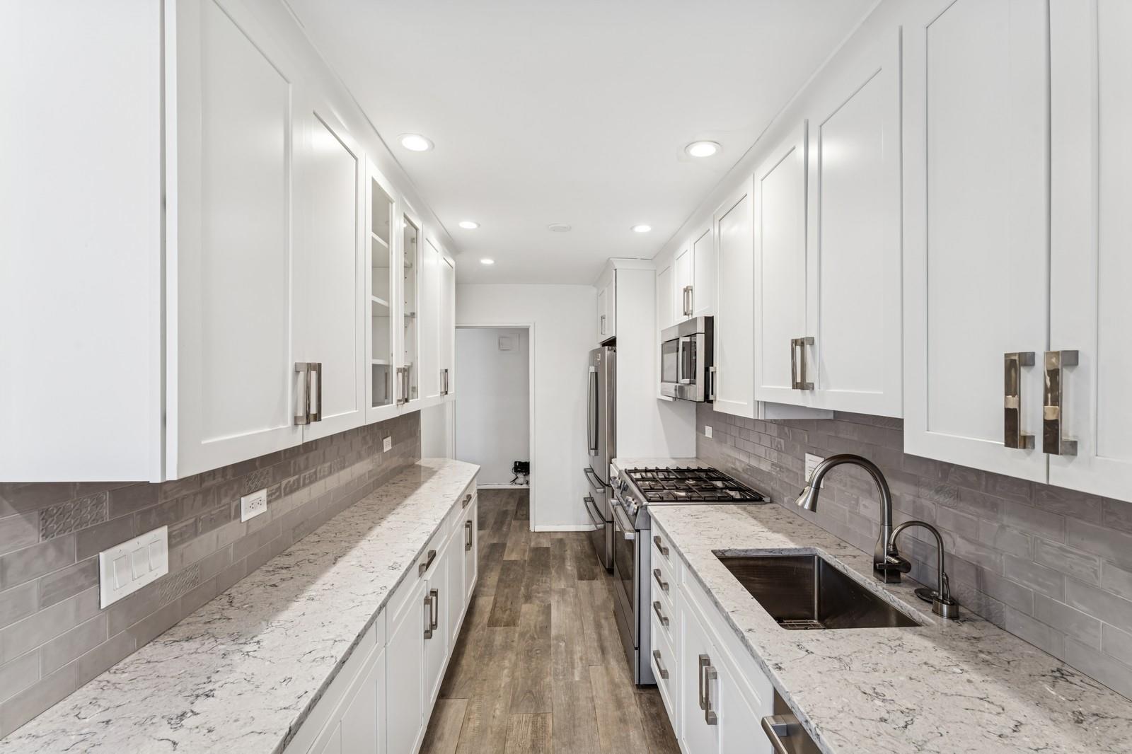 241-20 Northern Boulevard, Unit 2B Queens, NY 11362 - Photo 1 of 25 Kitchen featuring glass insert cabinets, white cabinetry, a sink, stainless steel appliances, and dark wood-style floors