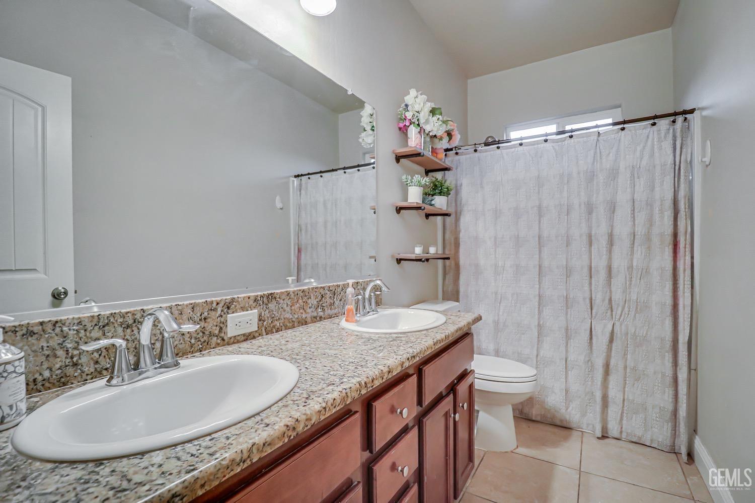 Undisclosed Address Bakersfield, CA 93313 - Photo 17 of 25 a bathroom with a granite countertop sink a toilet a mirror and shower curtain