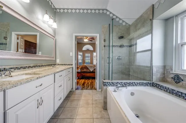 a spacious bathroom with a granite countertop tub sink a two mirror a window and a shower