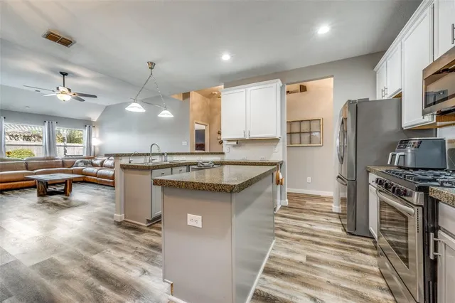 a kitchen with stainless steel appliances granite countertop a stove a sink dishwasher a refrigerator white cabinets and wooden floor