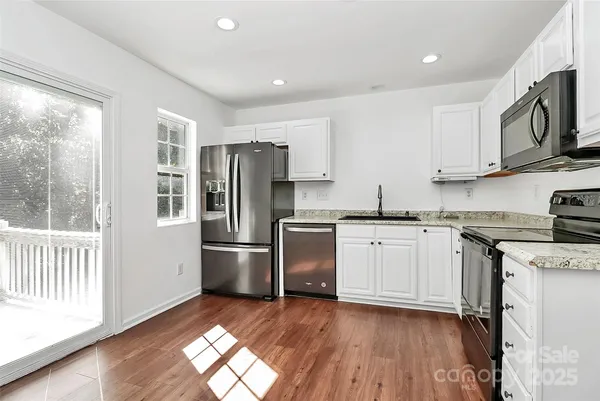 a kitchen with stainless steel appliances granite countertop a refrigerator a stove a sink and white cabinets with wooden floor