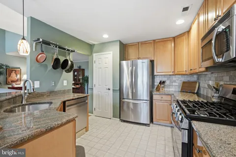 a kitchen with stainless steel appliances granite countertop a refrigerator a stove and a sink with wooden cabinets