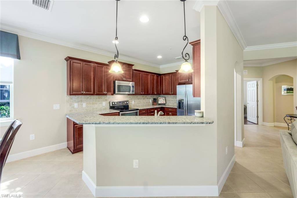 9532 Ironstone Terrace, Unit 102 Naples, FL 34120 - Photo 7 of 45 Kitchen featuring arched walkways, decorative backsplash, stainless steel appliances, light tile patterned floors, and ornamental molding