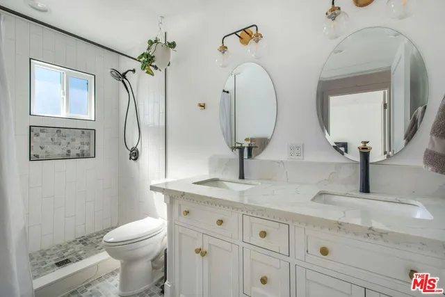a bathroom with double vanity sinks a toilet a mirror and shower