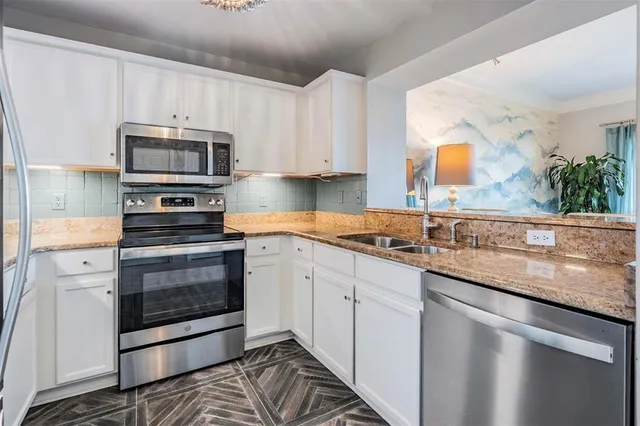 a kitchen with granite countertop a sink stainless steel appliances and white cabinets