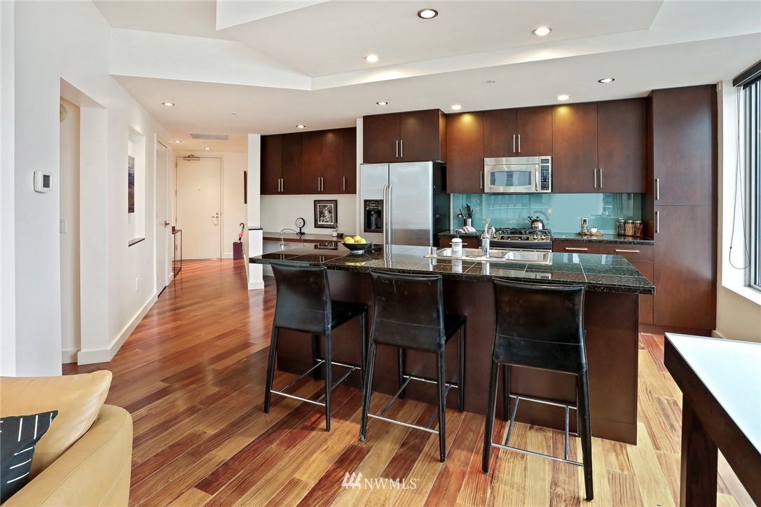 910 Lenora Street, Unit S1203 Seattle, WA 98121 - Photo 6 of 39 a kitchen with stainless steel appliances a dining table chairs sink and wooden cabinets